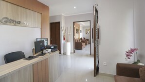 A reception area with a wooden reception desk, a computer, and a large vase with branches. - Capital O 2166 Elitya Stay (Denpasar)