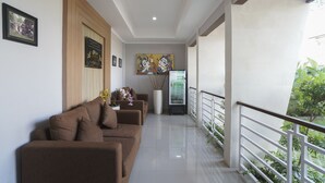 A modern living area with a brown sofa set, a white vase with flowers, and a refrigerator. - Capital O 2166 Elitya Stay (Denpasar)