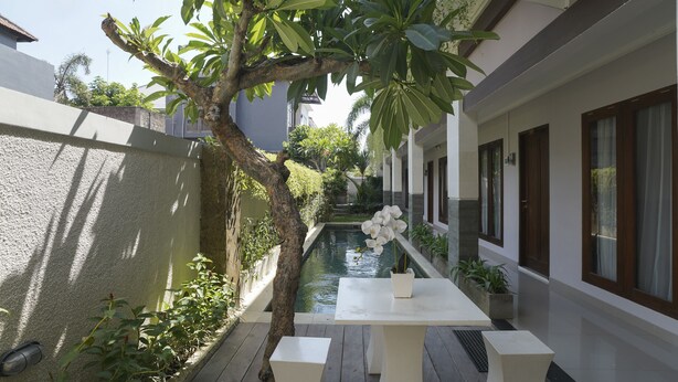 A narrow outdoor corridor with a small pool, white furniture, and a tree. - Capital O 2166 Elitya Stay (Denpasar)