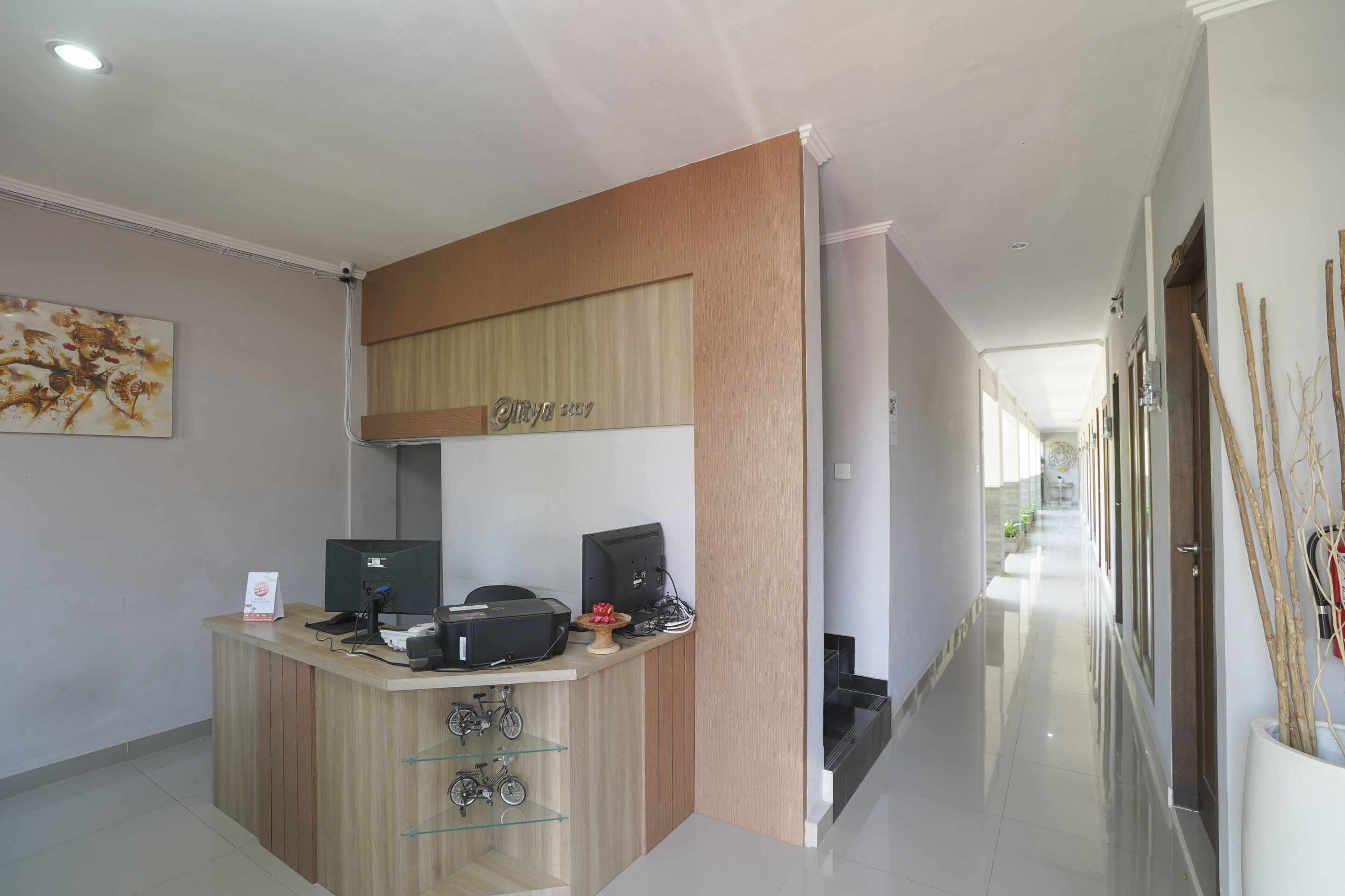 A reception desk with computers, a telephone, and a small decorative item. There is a sign on the desk and a framed picture on the wall.