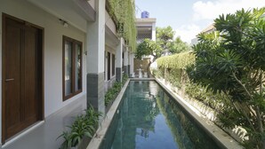 A narrow pool with a wooden door labeled "107" on the left, surrounded by plants and a building with a water tank in the background. - Capital O 2166 Elitya Stay (Denpasar)