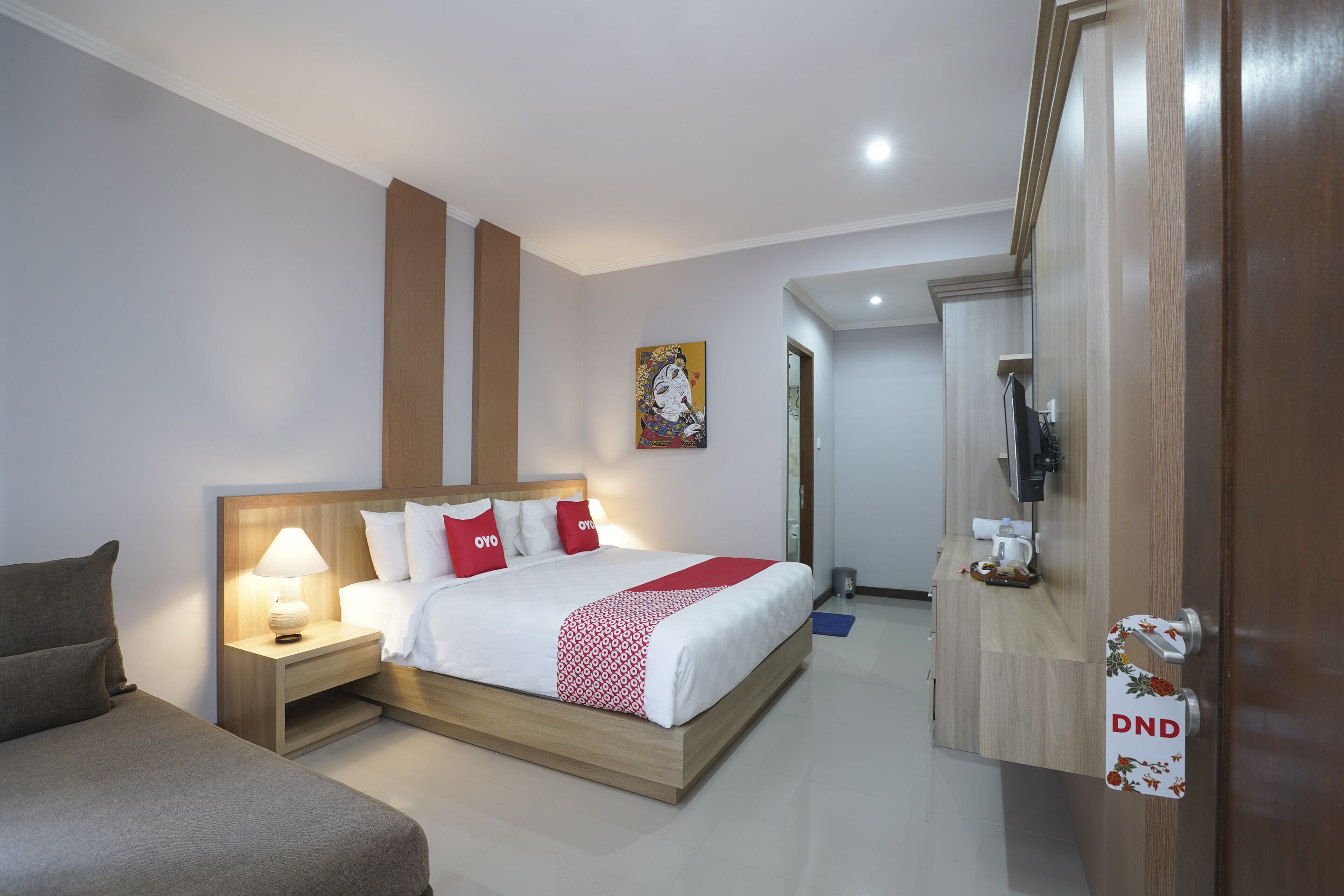 A hotel room with a bed, bedside tables, a lamp, a television, and a door with a sign.