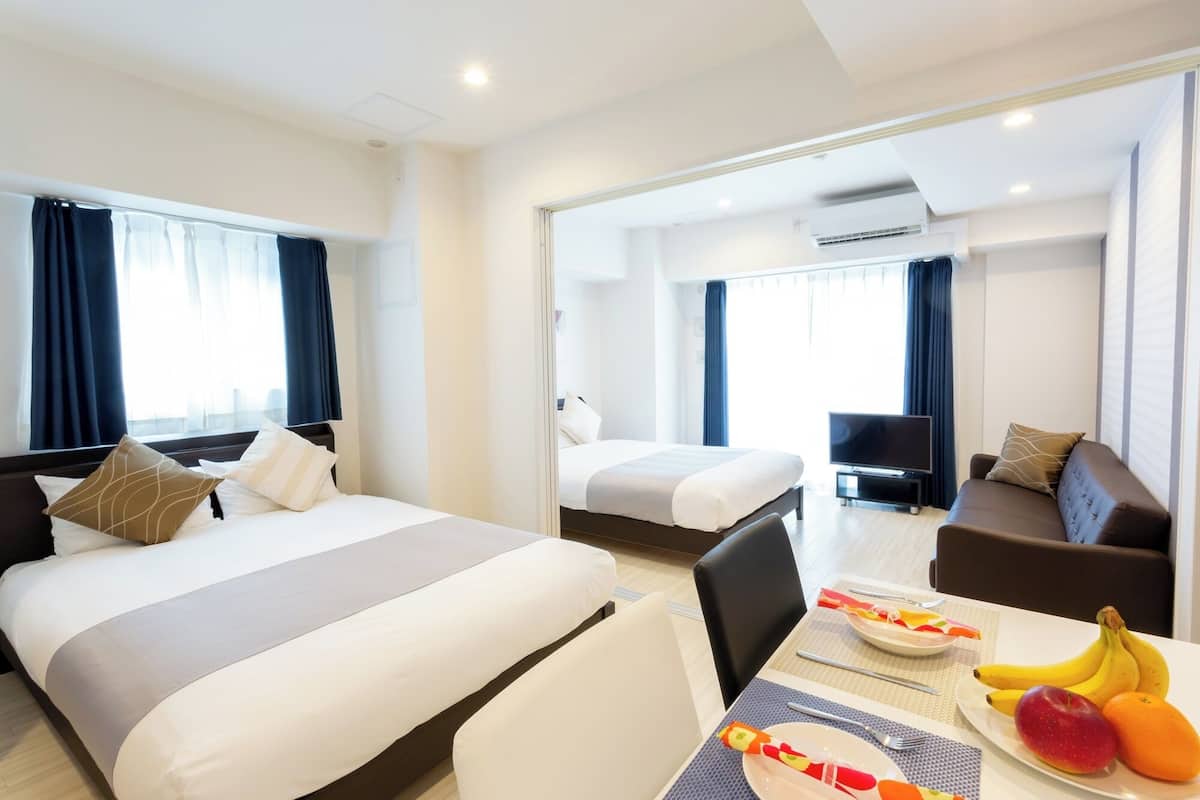 A hotel room with two beds, a TV, a dining table with fruit, and a mirror reflecting the room.