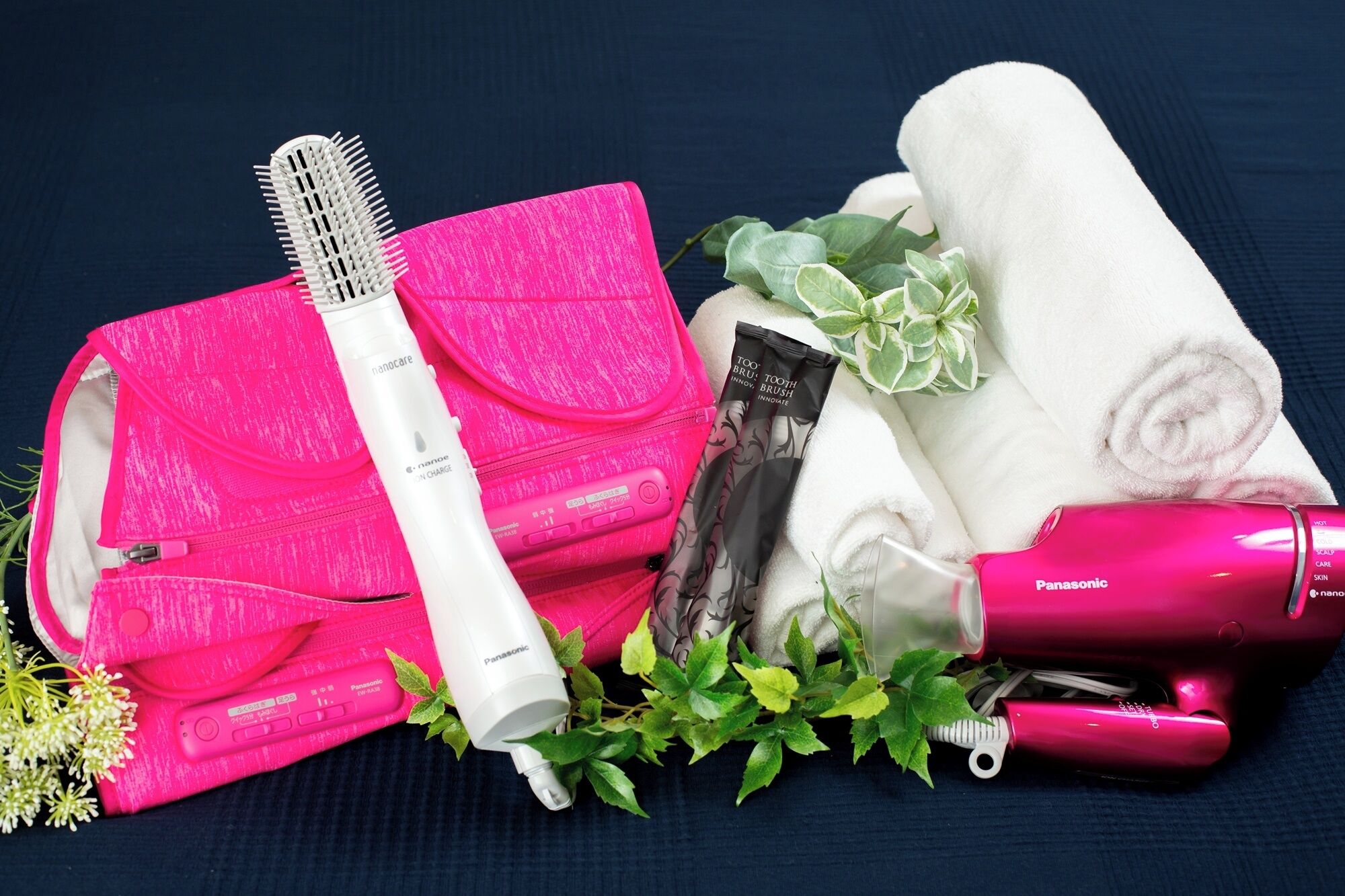 A pink hairbrush, a white hairdryer, a pink towel, a pair of black and white socks, and some green leaves.