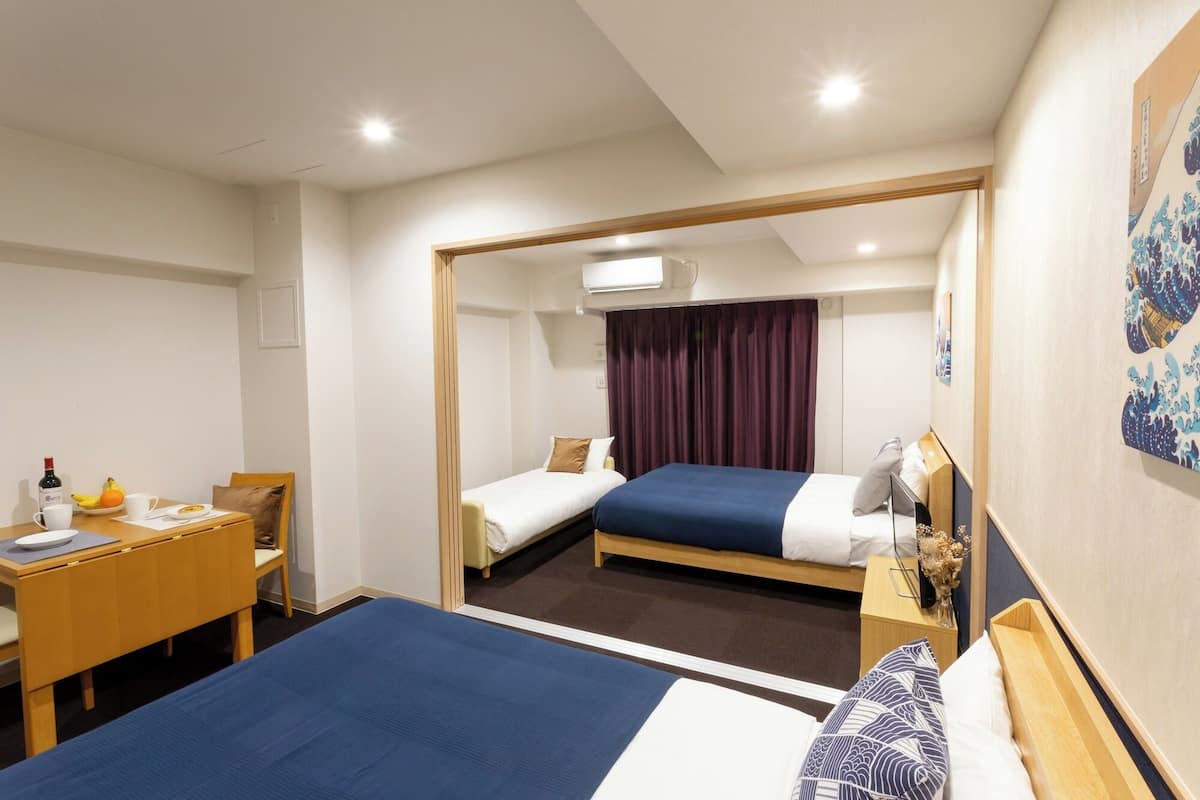 A hotel room with two beds, a desk, and a dining table.