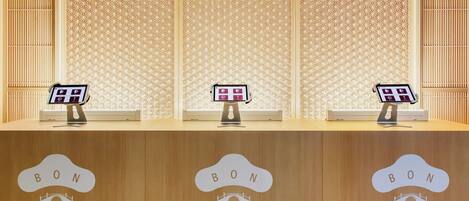A reception desk with three digital kiosks and a patterned wall in the background.