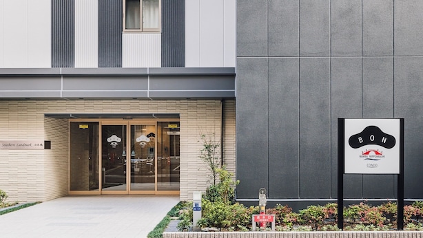 Une entrée d’immeuble avec des portes vitrées, une enseigne et un petit espace aménagé en jardin.