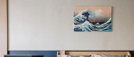 Habitación de hotel con cama, televisor sobre un soporte de madera y una pintura de una ola japonesa en la pared.