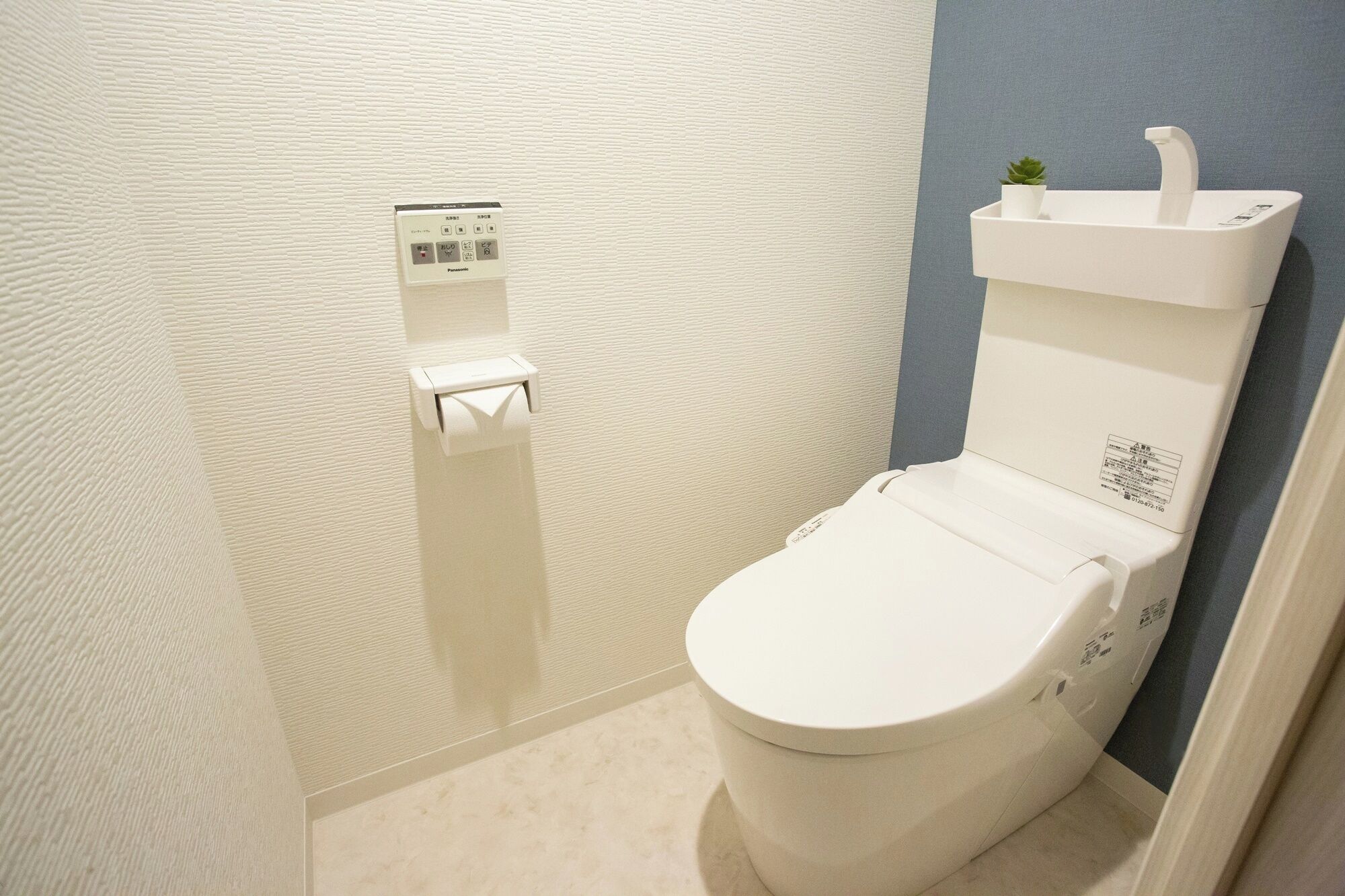 A modern bathroom with a toilet, a hand dryer, and a small potted plant on the sink.