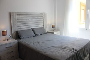 A bedroom with a bed, two bedside tables, a nightstand, and a window.