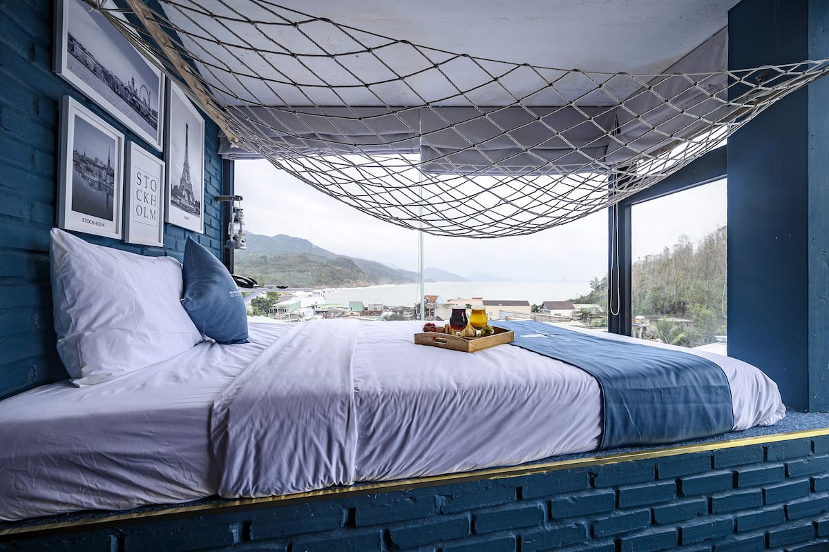 A bed with a view of the sea, framed by a blue wall and a netted ceiling.