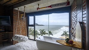 A room with a large window overlooking the ocean, a hanging chair, and a bathtub with fruits on the edge. - Mira Bai Xep Quy Nhon - The Hidden Jewel - Hostel (Quy Nhon Nam)