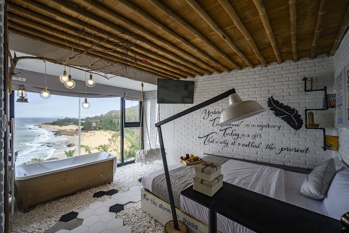 A bedroom with a view of the beach, a large window, a bathtub, and a wall with inspirational quotes.