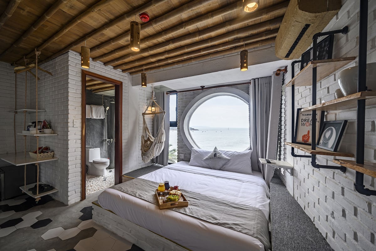 A bedroom with a bed, a breakfast tray, a window with a view, and a brick wall.