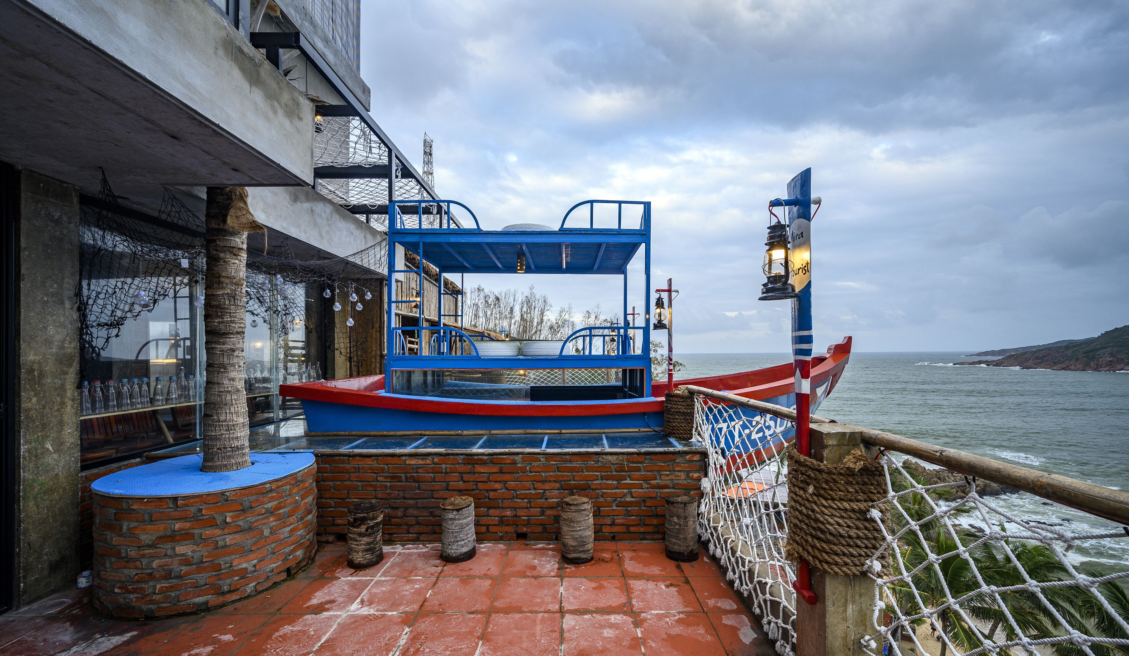 Un barco azul y rojo amarrado en un restaurante frente al mar, con vista al océano y un cielo nublado.