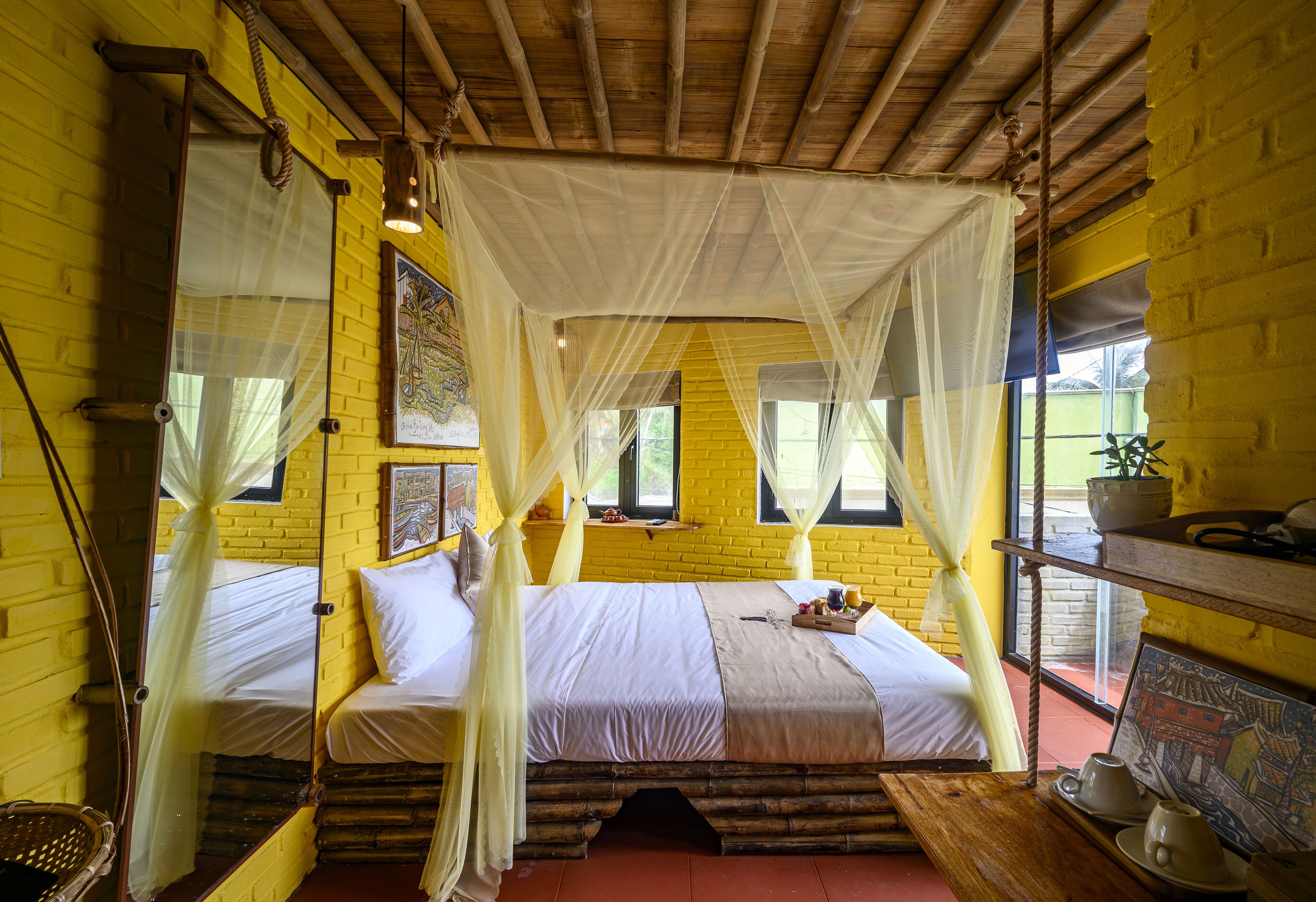 A room with a bed, a wooden bench, a shelf with items, and a window with a view.