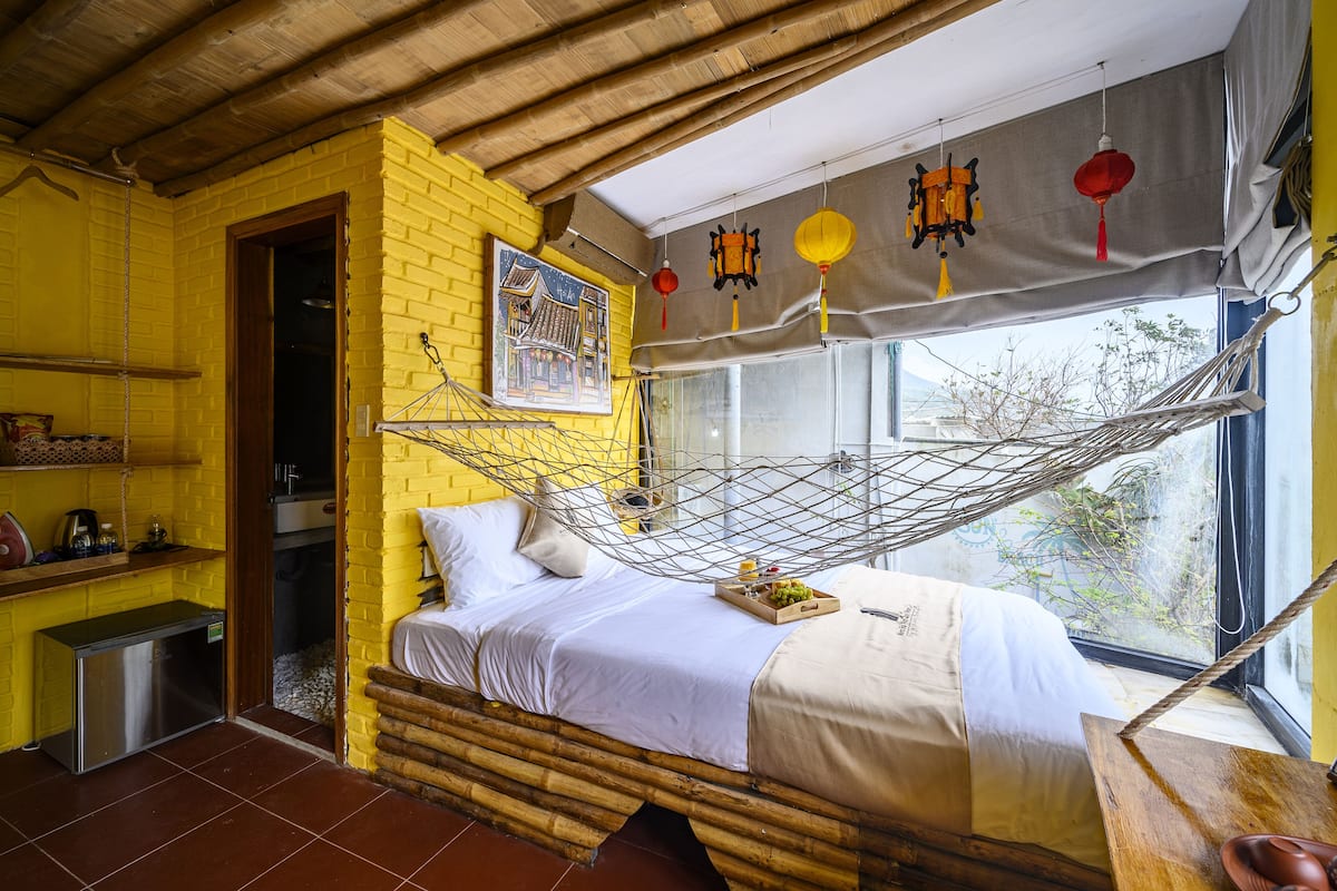 A room with a bed, a hammock, a small kitchen area, and a window with a view.