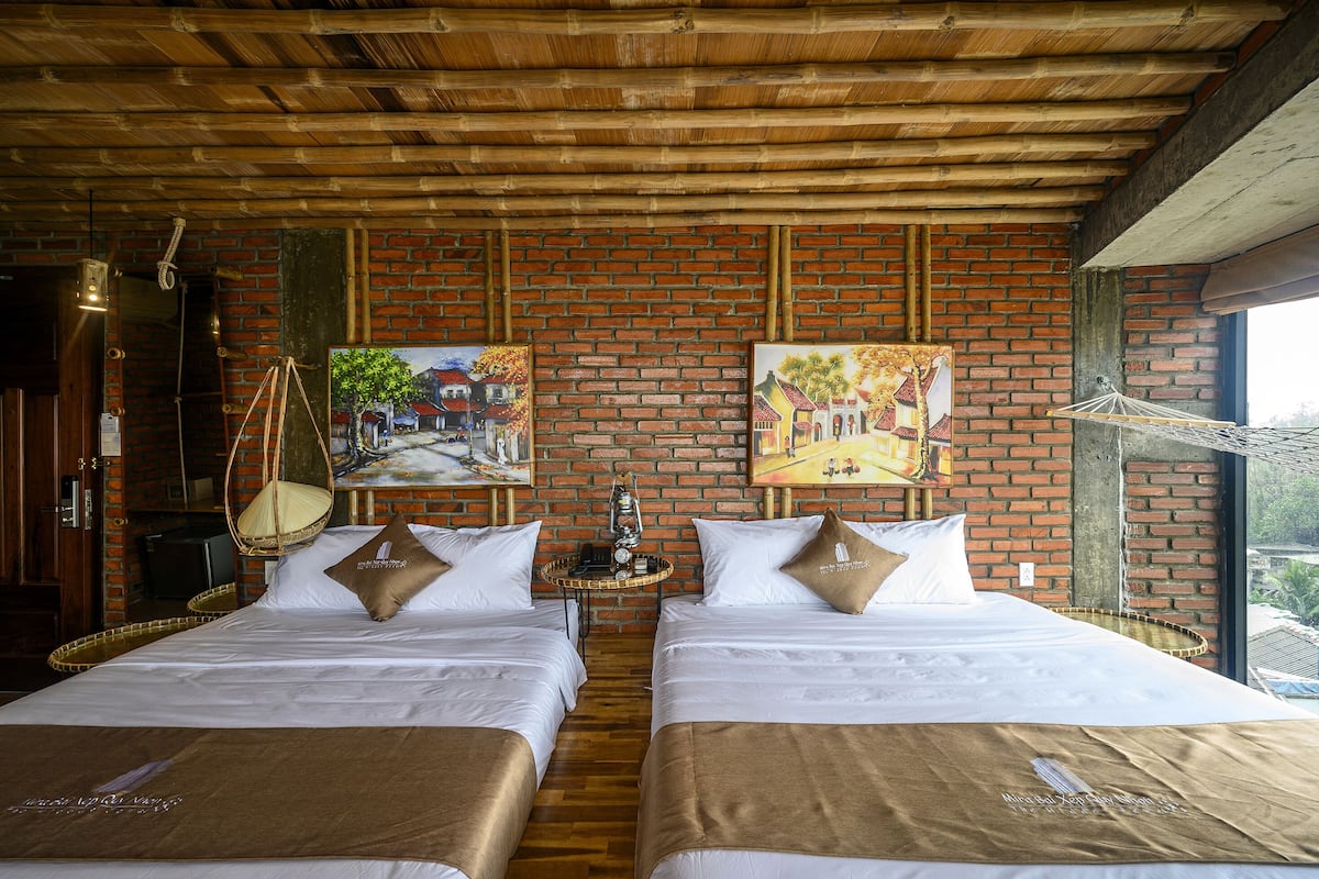 A hotel room with two beds, a brick wall, and artwork.