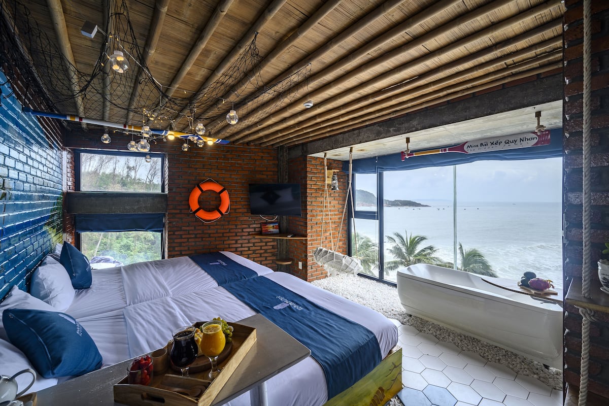A room with a large bed, a bathtub, and a view of the sea.