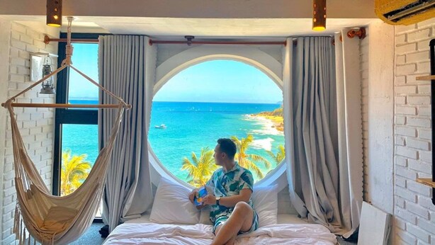 A room with a large window, a hammock, and a bed with a view of the sea. - Mira Bai Xep Quy Nhon - The Hidden Jewel - Hostel (Quy Nhon Nam)