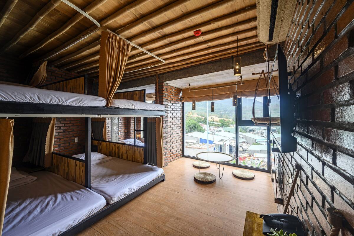 A rustic room with bunk beds, a brick wall, and a large window offering a city view.