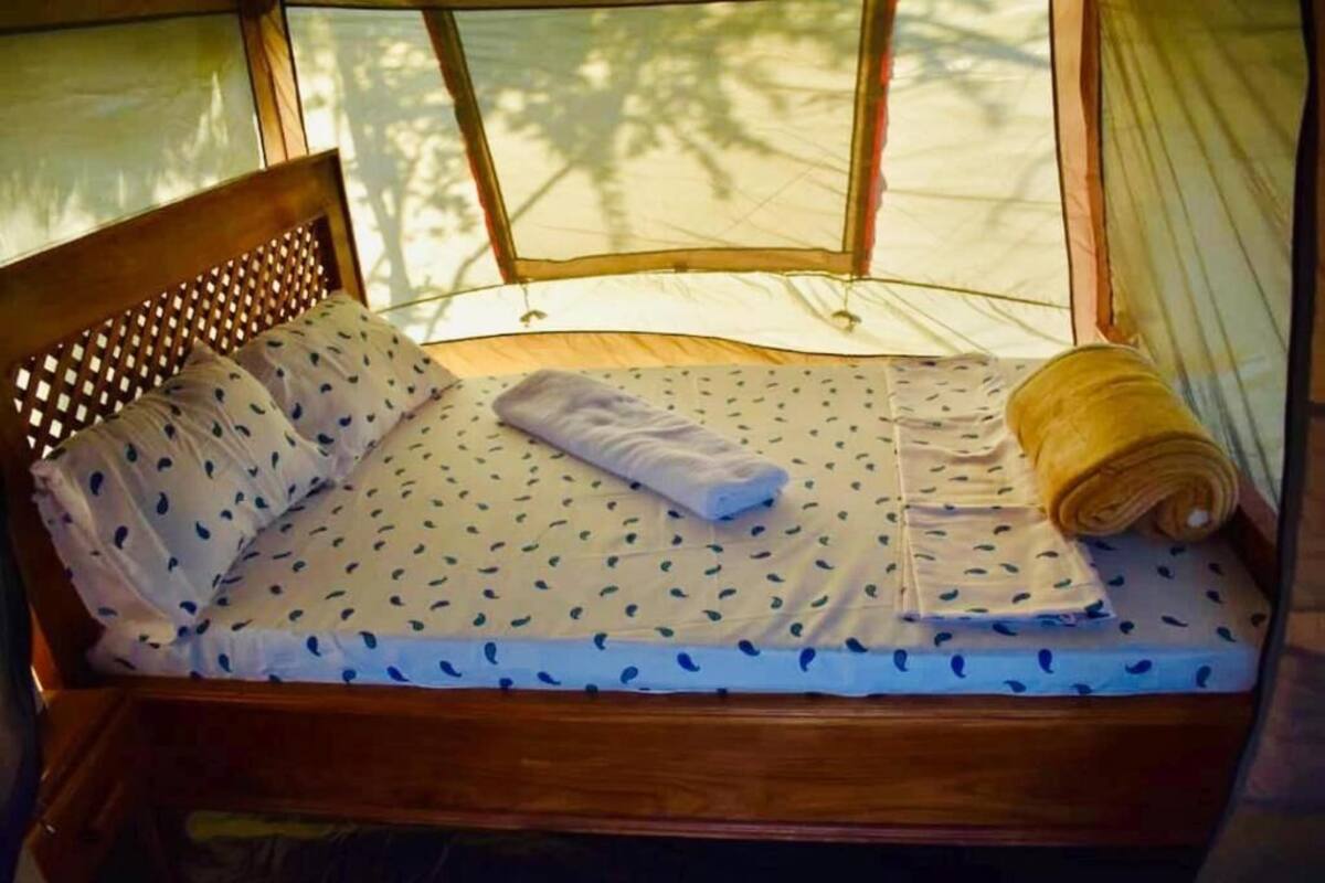 Una cama con cabecera de madera, una colcha blanca con motivos azules y una toalla enrollada.