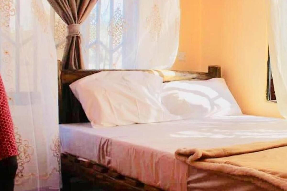 Una cama con sábanas blancas, una manta color beige y un cabecero de madera.