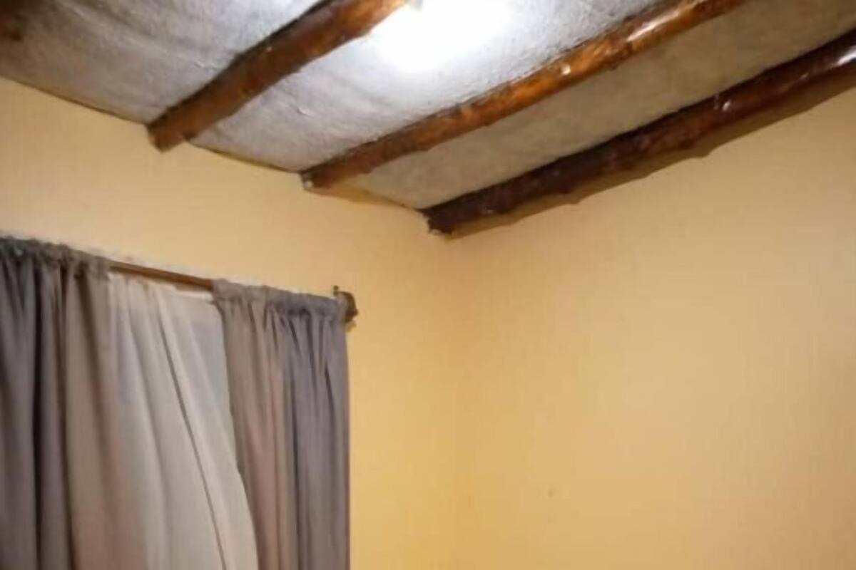 Una cama individual con estructura de madera y ropa de cama blanca en una habitación con pared amarilla lisa y una viga de techo de madera.