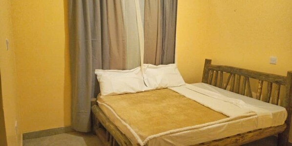 A single bed with a wooden headboard, a white mattress cover, and a beige blanket. - Ritungu Camp (Morogoro)
