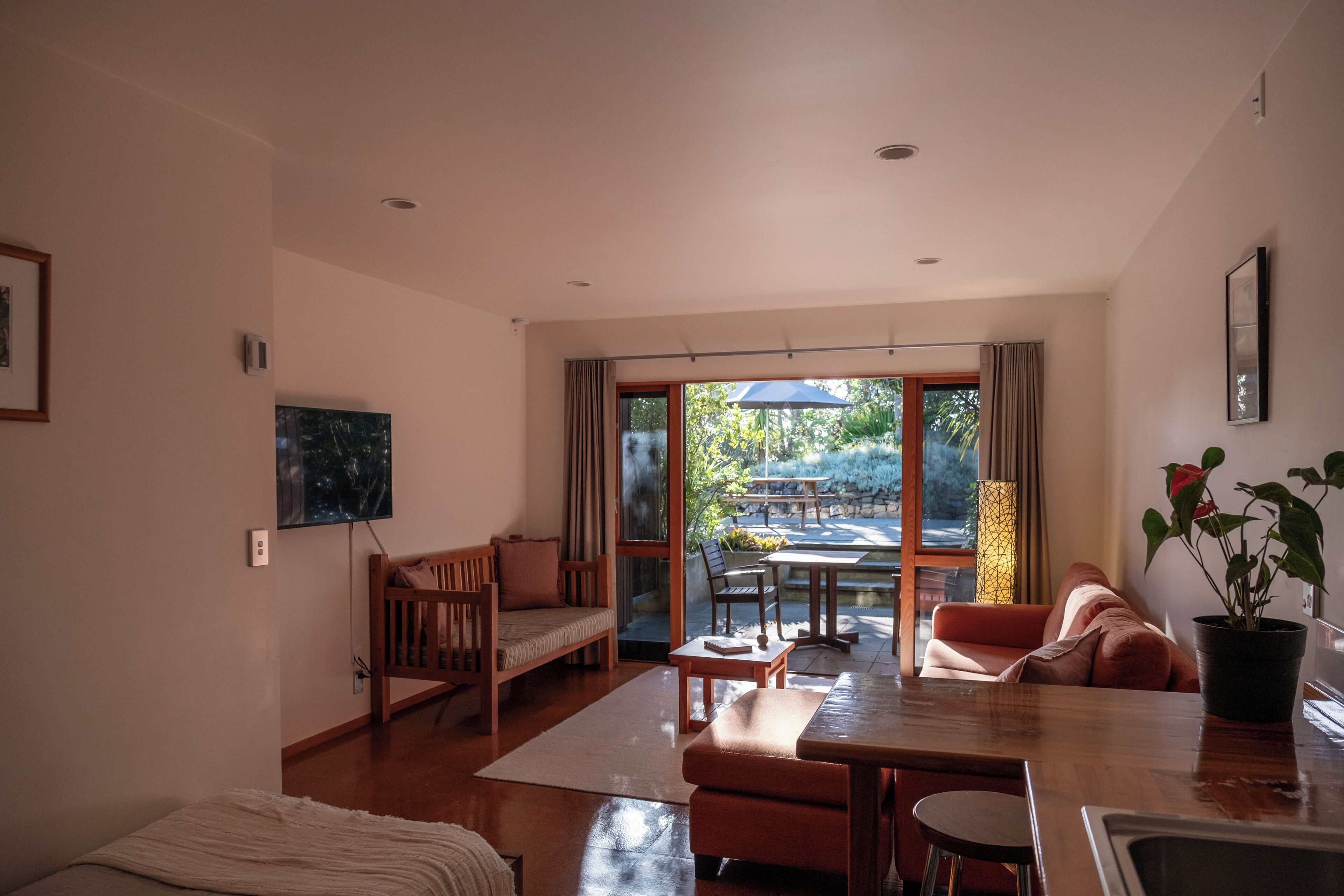 A spacious living area with a wooden bench, a sofa, and a dining table. There is a large window providing a view of the outdoors.