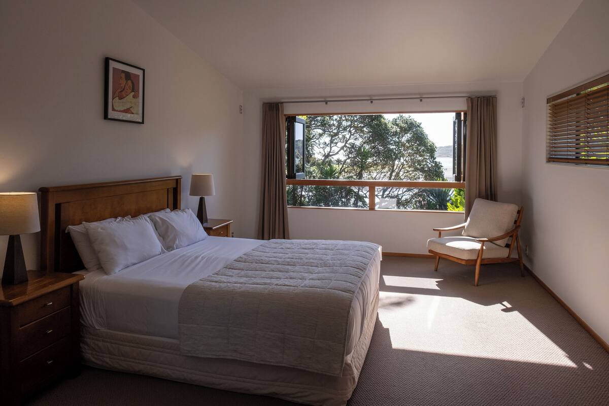 Un dormitorio con una cama grande, una silla, una mesita de noche y una ventana con cortinas.