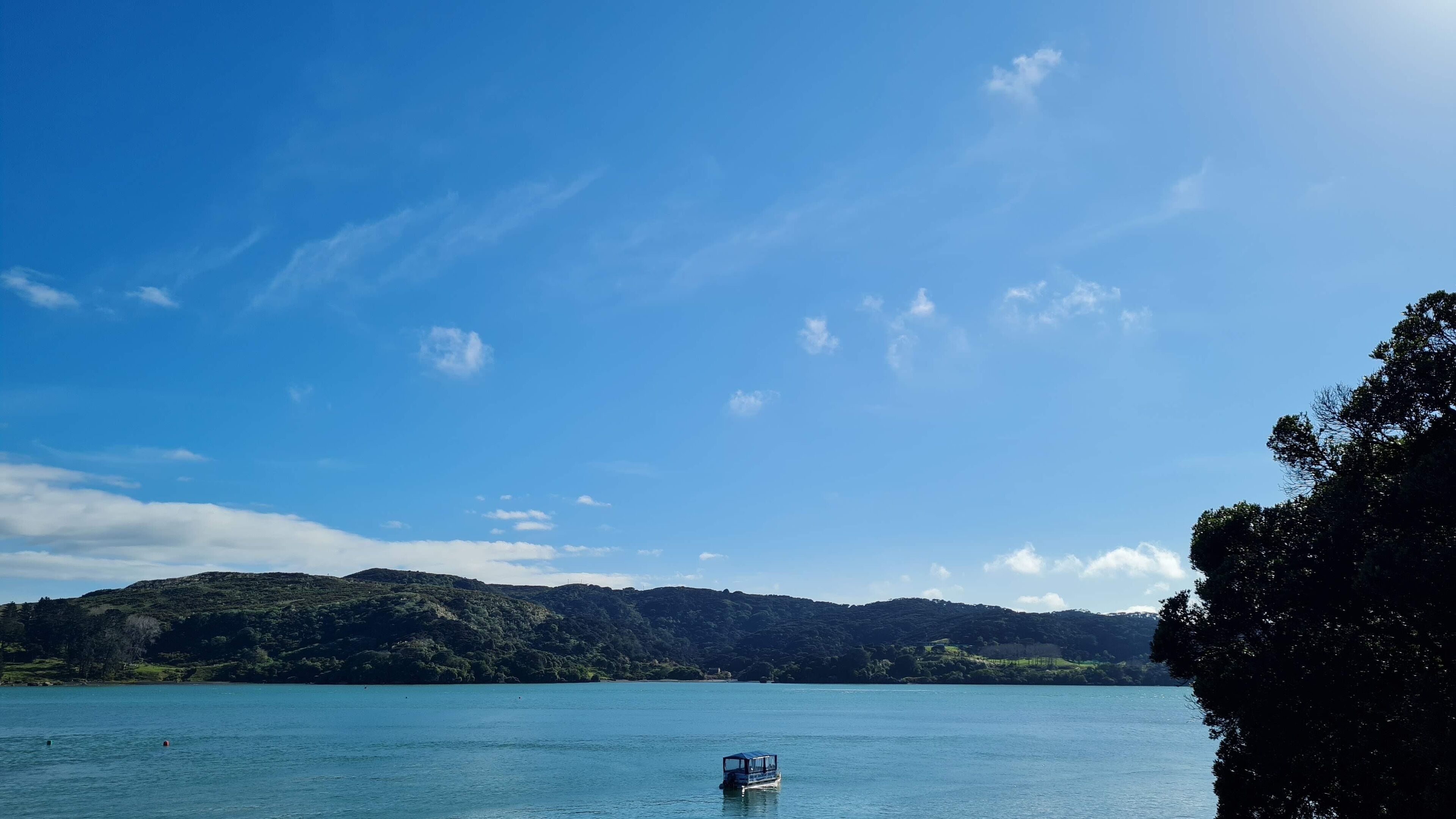 A calm lake with a small boat in the foreground and a forested hill in the background.