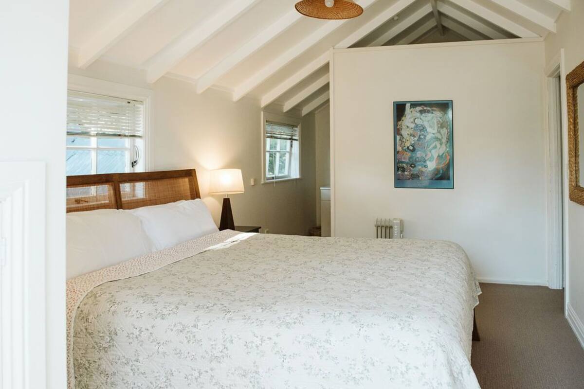 Un dormitorio con una cama grande, una mesita de noche, una lámpara, un cuadro en la pared y una ventana con persianas.