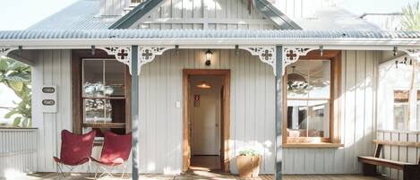 Ett vitt trähus med en veranda, två röda stolar, en träbänk och en krukväxt.
