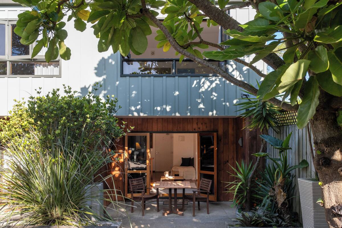 Una casa moderna con terraza de madera, un comedor con sillas y vista al jardín trasero.