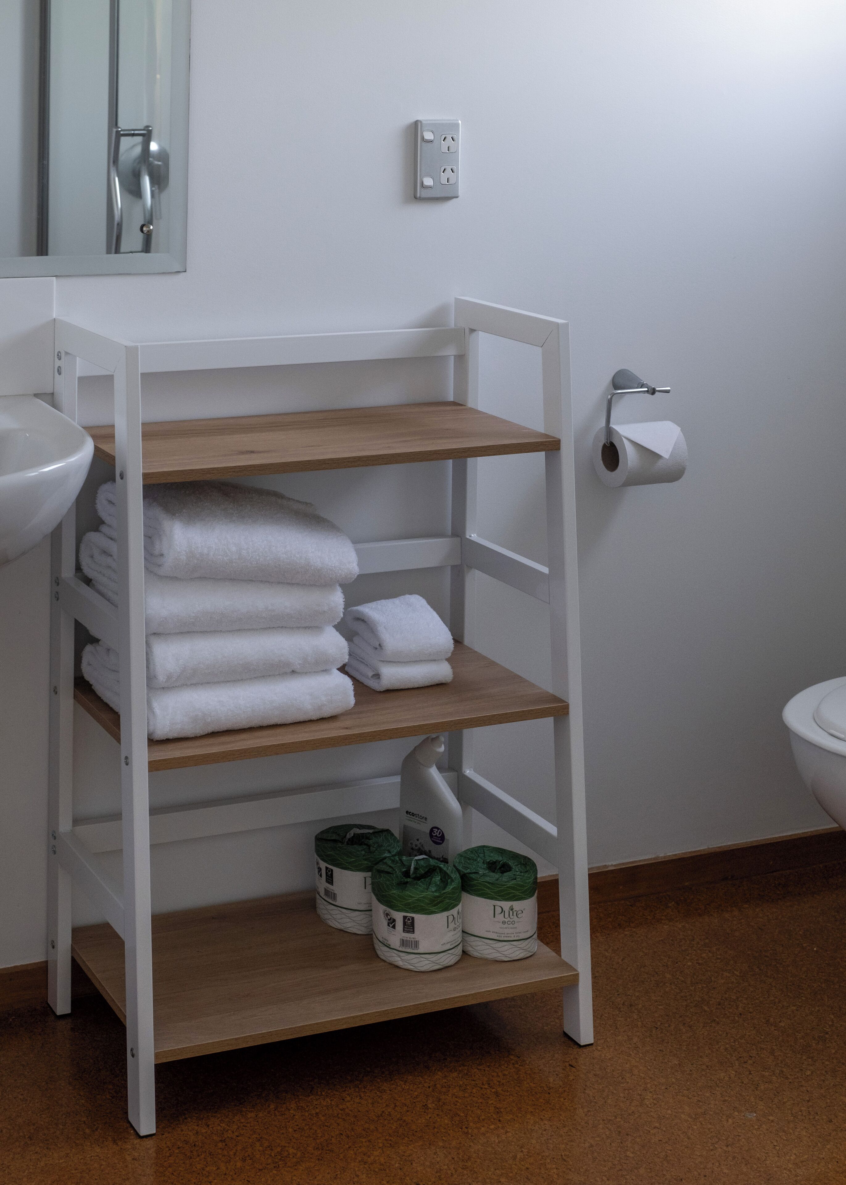 A bathroom with a white shelf holding towels, a toilet paper holder, and toilet paper.