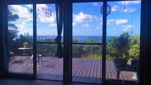 A room with large sliding glass doors leading to an outdoor deck with a view of the ocean and surrounding greenery. - Galaxy Guest House (Hachijo)