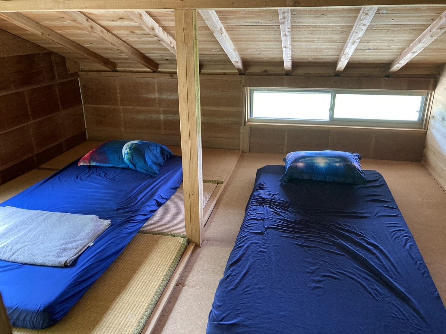 A small, single-room cabin with two bunk beds, a window, and a wooden ceiling.