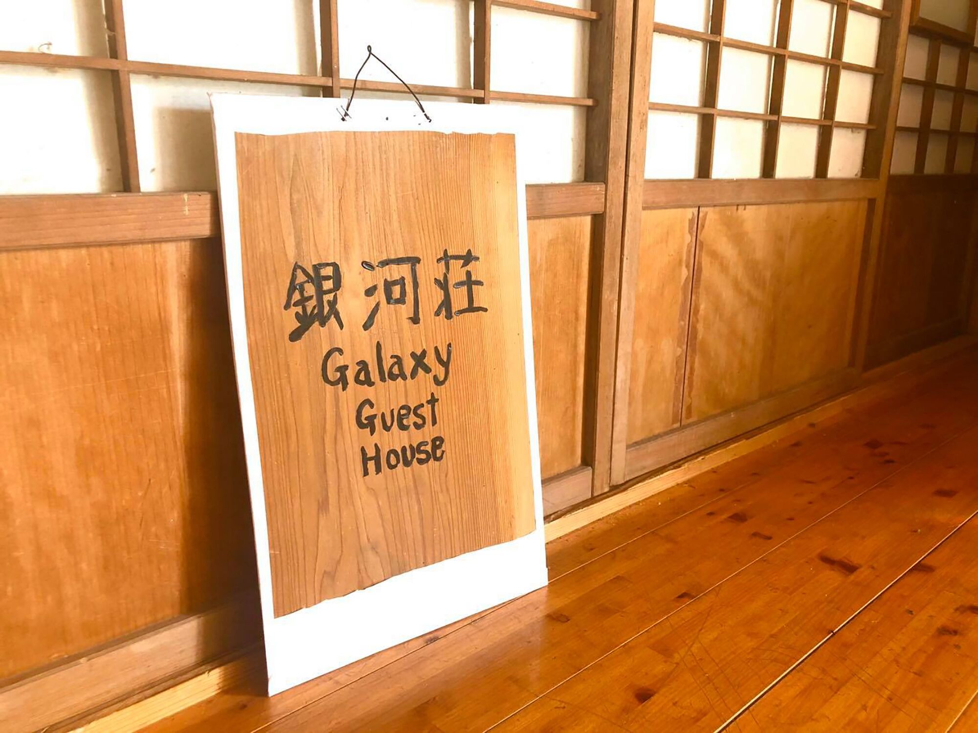 Un letrero de madera con el texto 'Galaxy Guest House' en inglés y otro idioma.