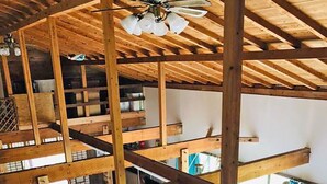 A multi-level wooden structure with a ceiling fan, a sofa, and potted plants. - Galaxy Guest House (Hachijo)