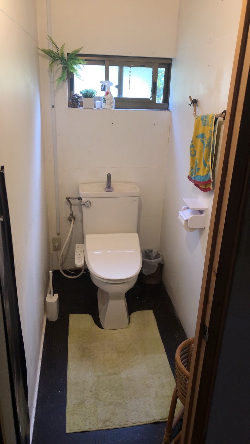 A compact bathroom with a toilet, a small sink, a window, and a plant.