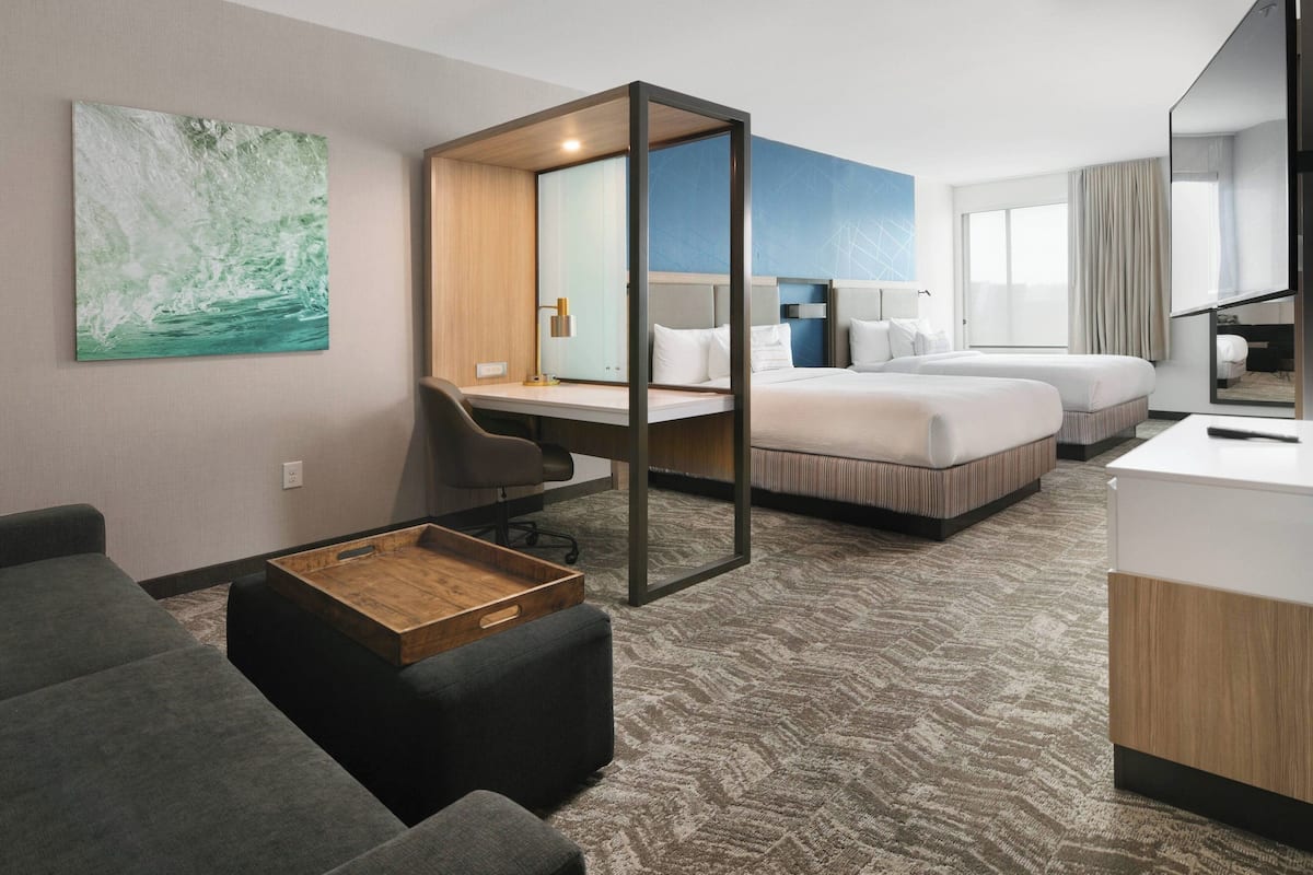 Una habitación de hotel con cama, escritorio, silla, mesita y un espejo grande.