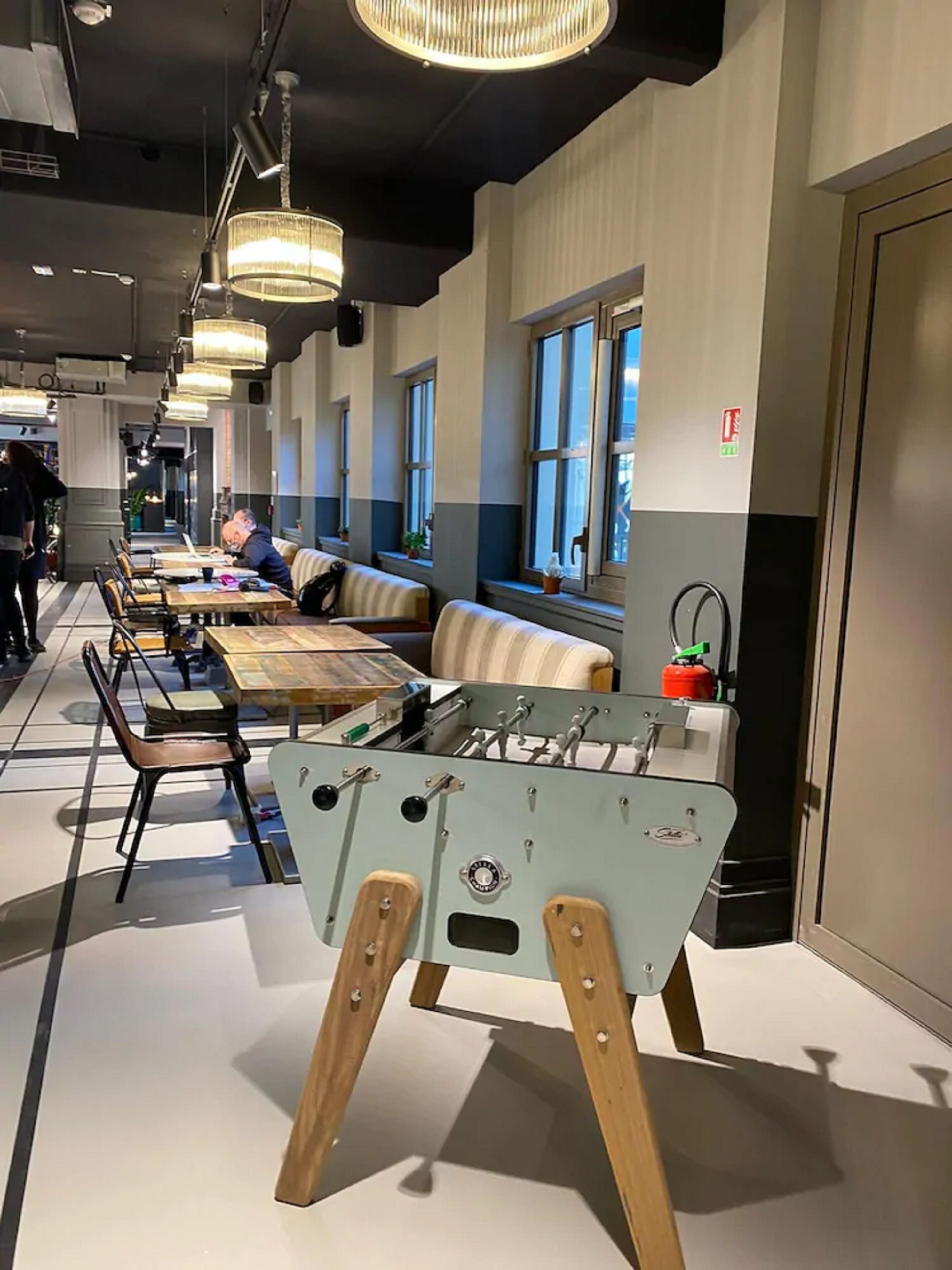 A modern dining area with tables and chairs, a foosball table, and large windows.