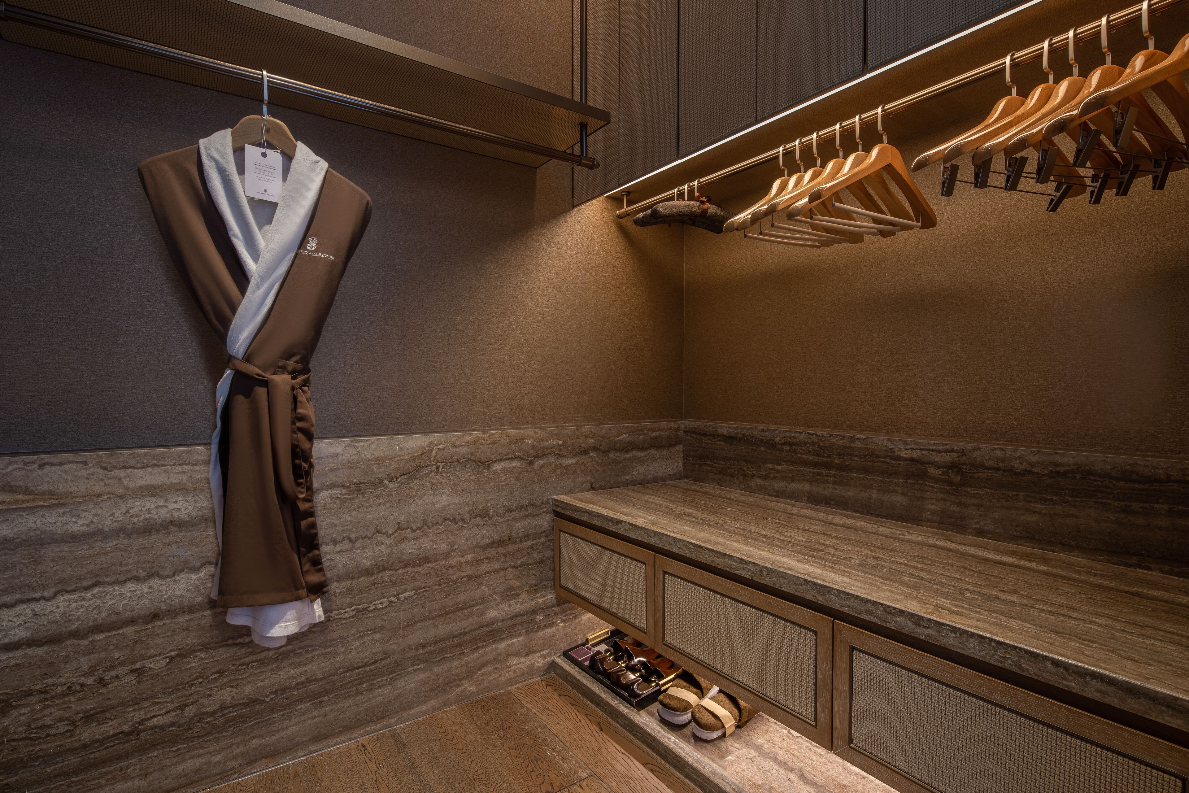 A modern bathroom with a robe hanging on a rack, a shower area, and a bench with shoes.