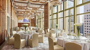 A spacious banquet hall with high ceilings, large windows, and elegant chandeliers. Tables are set for dining with chairs and centerpieces.
