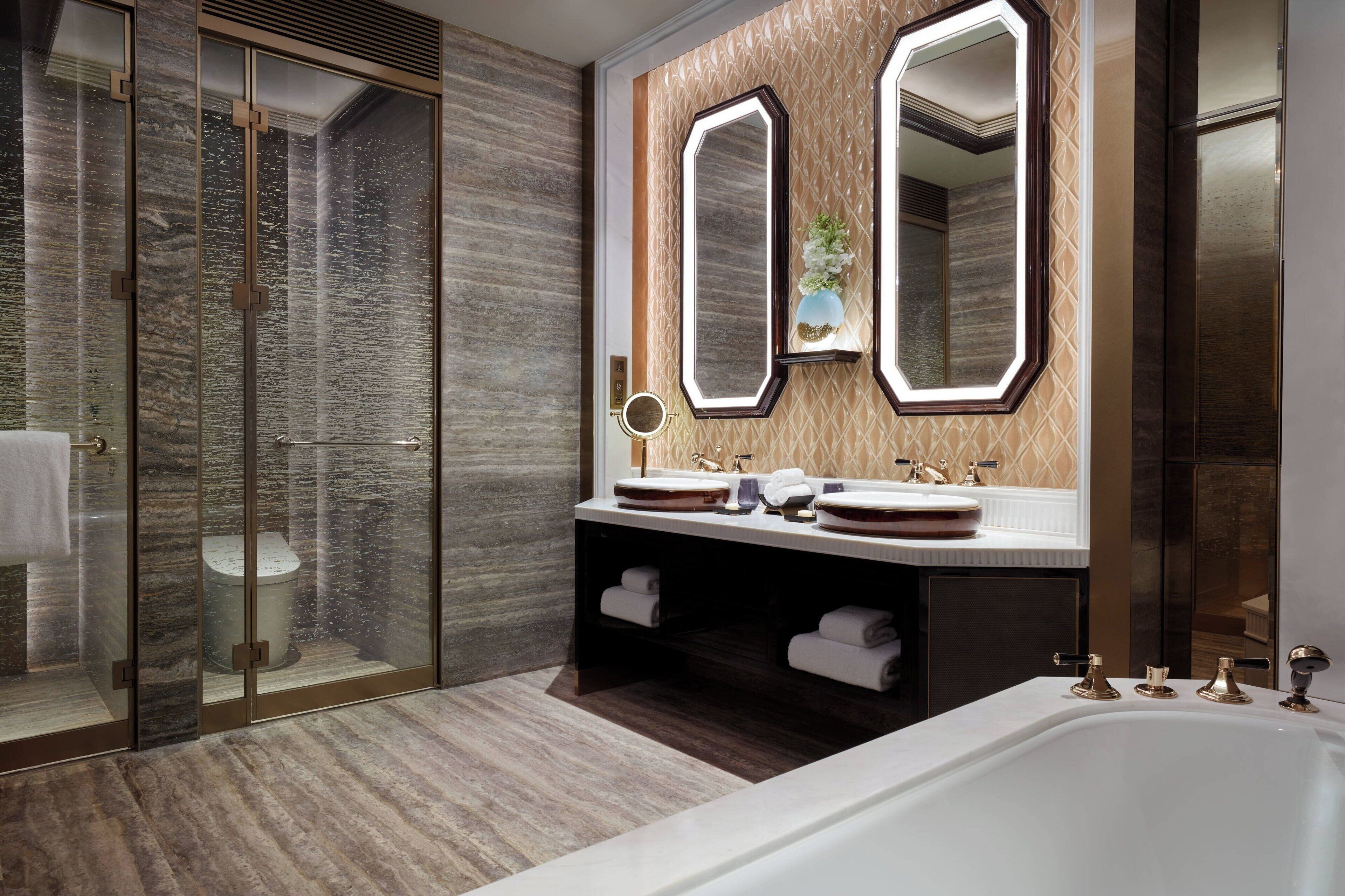A modern bathroom with a glass-enclosed shower, dual sinks with round mirrors, and a large bathtub.