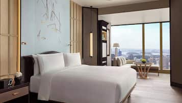 A modern hotel room with a large bed, a view of the city, and a small table with a lamp.
