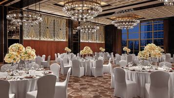 A banquet hall with round tables, white chairs, and chandeliers.