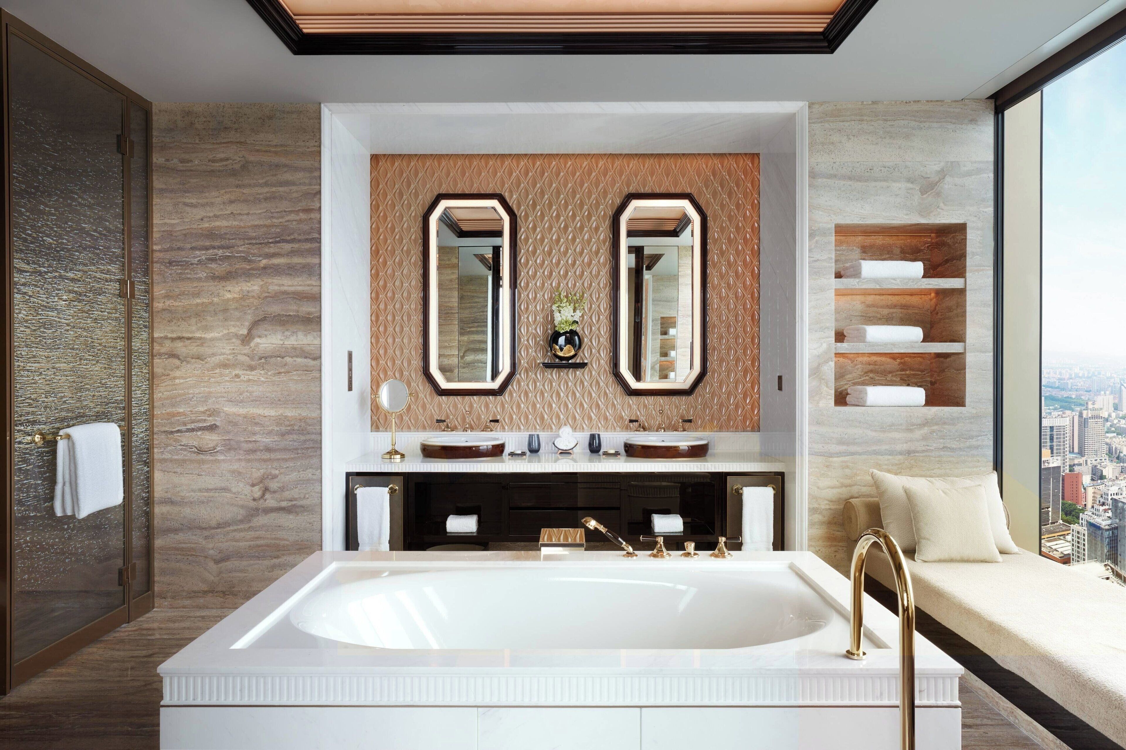 A modern bathroom with a large bathtub, two mirrors, and a city view.