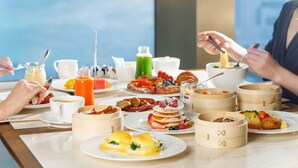 A breakfast buffet with various dishes, including pancakes, omelets, and pastries, served on a marble table.